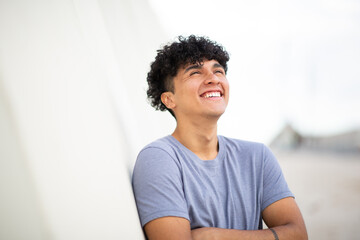 happy young man laughing with arms crossed by white wall