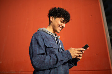 Side of smiling young man using mobile phone by red wall