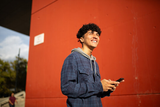 smiling young man with mobile phone by red wall