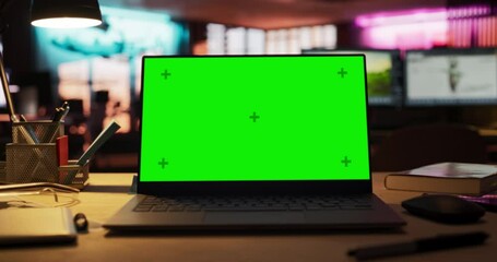 Laptop Computer with Green Screen Standing on a Wooden Desk with Height Adjustable Function. Chroma Key Display in Empty Decorated Creative Office for Game Development Startup. Zoom In Shot