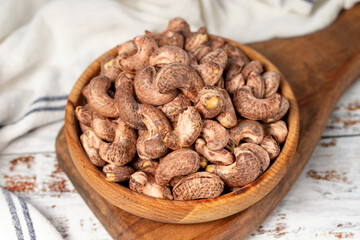 Cashews with shell in wood bowl. Shelled cashew on white wood background. Close up