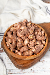 Cashews with shell in wood bowl. Shelled cashew on white wood background