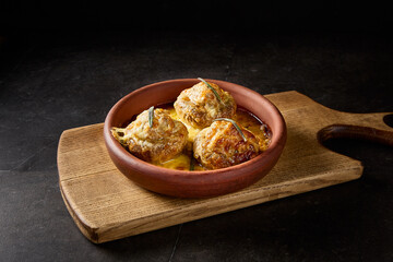 Baked mushrooms stuffed with meat on a rustic clay plate, beautifully presented on a wooden board against a minimalist black backdrop, showcasing traditional Georgian cuisine