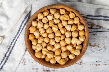 Roasted hazelnuts in wood bowl. Peeled hazelnuts kernel on white wood background. Top view