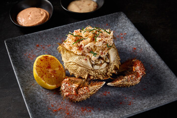 Horizontal close-up of cleaned crab meat with lemon, presented in a hairy crab, with sauces on a gray stone plate, black background