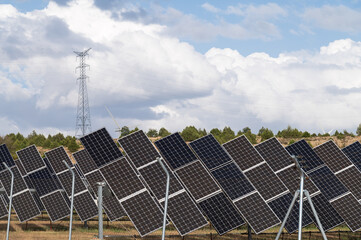 Vista de un huerto solar con placas fotovoltaicas orientables y una torre eléctrica al fondo.