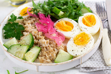 Breakfast oatmeal porridge with boiled eggs, cucumber, red onion and greens. Healthy balanced food.