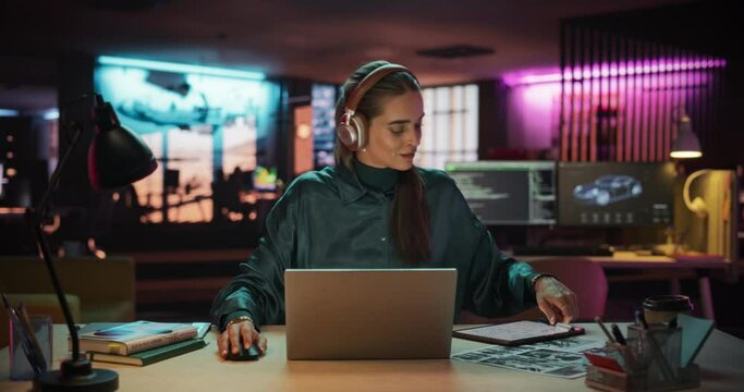Young Project Manager with Headphones Working on Laptop Computer in Creative Office Environment. Beautiful Female Specialist is Writing Business Strategy, Using Digital Tablet to Take Notes