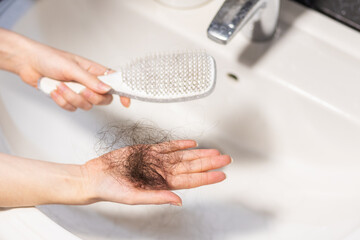 Close-up of woman's hands holding comb over sink and shows big clump of lost hair lies on palm. Concept of baldness and alopecia - obrazy, fototapety, plakaty