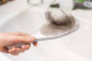 Close-up of female hand holding comb with big clump of lost hair over sink. Concept of baldness and alopecia