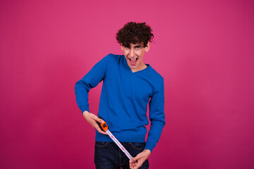 Young attractive student measuring length and posing against pink background.