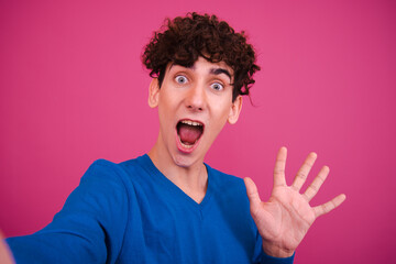 Young attractive curly man posing on a pink background.