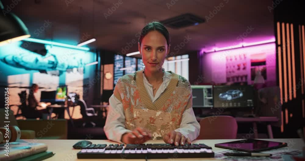 Poster pov from monitor screen: portrait of a woman using desktop computer in a creative agency lit by neon