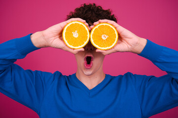 Young attractive curly man posing on a pink background and eating an orange.