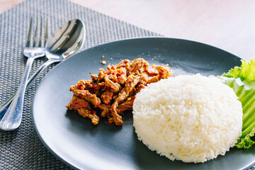 Steamed rice and beef stir-fry with salt and pepper in black plate on dining table.