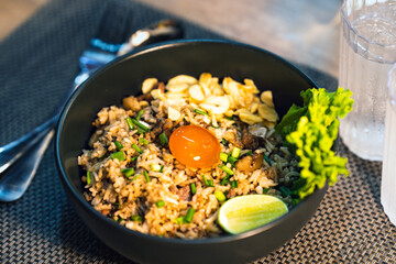 Beef fried rice with egg yolk on top in a black bowl on a restaurant table.