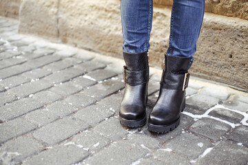 Women's legs in blue jeans and black leather winter boots. Stylish winter footwear