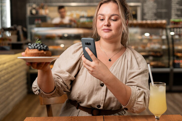 Influencer and also blogger using smartphone to take a photo of brownie before eating breakfast in the cafe