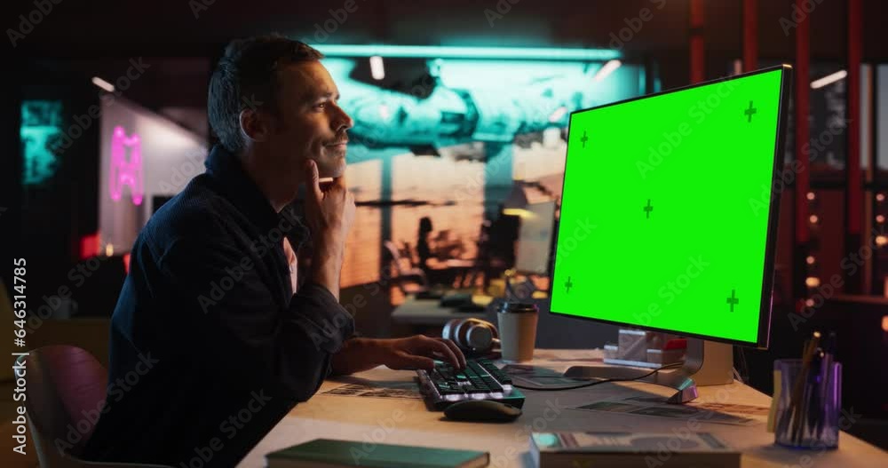 Poster Portrait of Young Man Sitting at His Desk Using Desktop Computer with Mock-up Green Screen. Male Caucasian Specialist Working on Computer with Chroma Key Display at Creative Agency