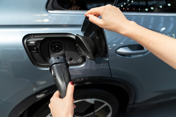 Woman holding plug of electric car charging station.
