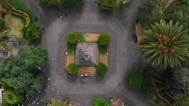 Aerial Pull Out Drone Shot Over Juan Montalvo Statue with a Flock of Birds Flying Below.