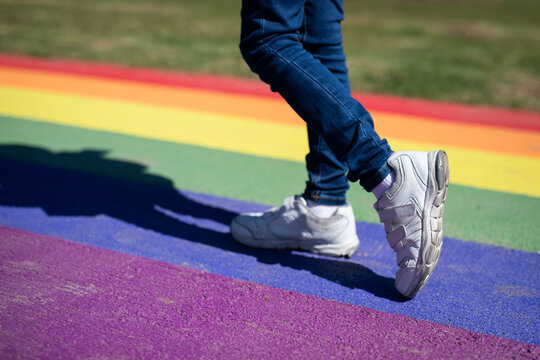 young child feet white sneakers walking colorful rainbow pride shadow sun grass casual jeans joggers walk