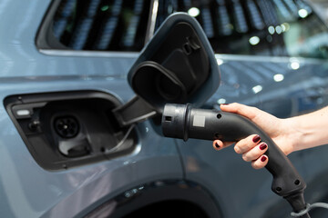 Woman holding plug of electric car charging station.