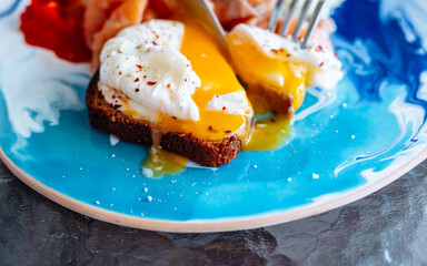 Salmon, vegetables and poached egg. Delicious healthy breakfast plate. Fork and knife slicing yolk on blue plate