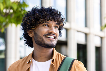 Close-up photo of a young Indian smiling man looking to the side with a confident look. Standing...