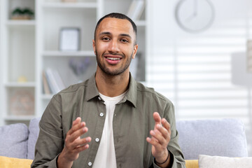 Young hispanic man conducts online training, seminar via video call from home. He looks at the...