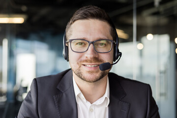 Close-up photo of a young male teacher wearing a headset and suit sitting in front of the camera...