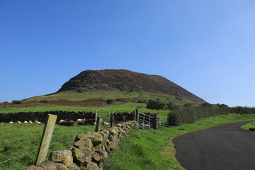 Slemish Mountain viewed from roadside against backdrop of blue sky on late summer day. County Antrim, N. Ireland