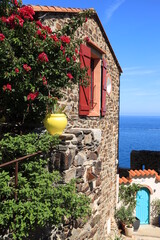Stone house adorned with flowers and featuring brightly coloured doors and window shutters in Mediterranean seaside town of Collioure, southern France