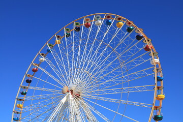 Fototapeta premium Ferris wheel featuring colourful seating pods against backdrop of blue sky