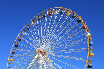 Ferris wheel featuring colourful seating pods against backdrop of blue sky