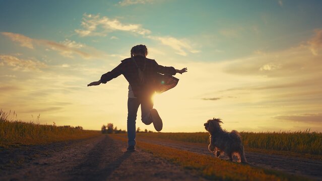 teen girl running with a dog in the park. happy family freedom a kid dream concept. silhouette of a teenage girl running along the road in the park at sunset view from the back sun with a shaggy dog