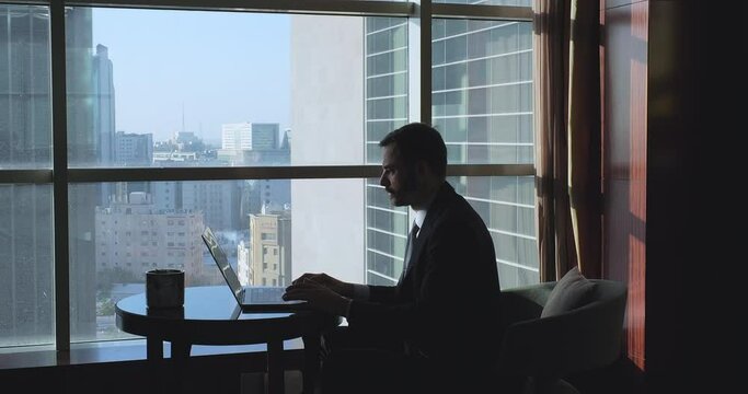 Silhouette of businessman working in the hotel room near the windows overlooking the city. Business meetings abroad concept