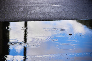 a puddle on the asphalt with a reflection of the blue sky during when it rains.