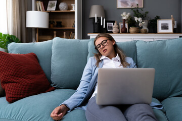 Young business woman fell asleep on sofa while working on laptop. Overworked tired woman tired of...