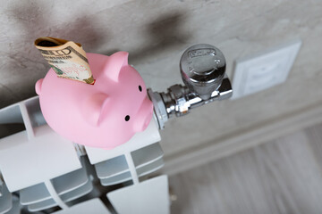 Savings concept.Money in piggy bank on radiator on a gray wall background. Concept of heating...