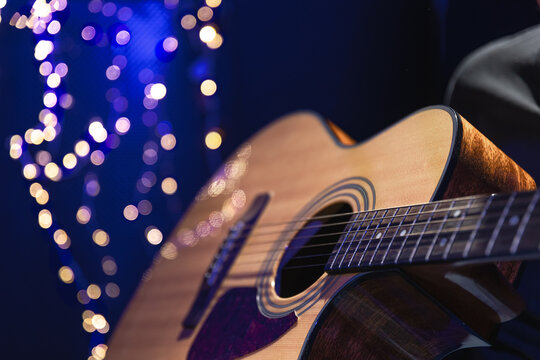 Close-up, acoustic guitar on a dark background with bokeh lights.
