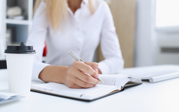 Female hand holding silver pen ready to make note in opened notebook sheet. Businesswoman coffee cup workspace make thoughts records at personal organizer white letter collar conference signature