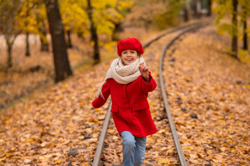 Caucasian girl in a red coat and beret walks along the railway tracks in the park in autumn.