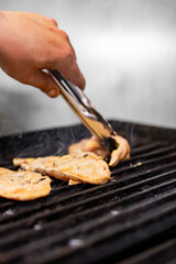 Chef grilling chicken fillet on hot pan in a restaurant kitchen