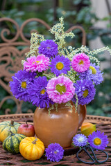 Blumenstrauß mit pink und lila Astern in einer rustikalen Vase im Garten