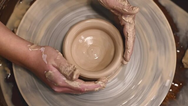 Potter girl works on potter's wheel, making ceramic pot out of clay in pottery workshop. Art and hobby concept. slow motion