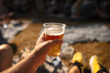 Person holding beer cup outdoors on a sunny day.