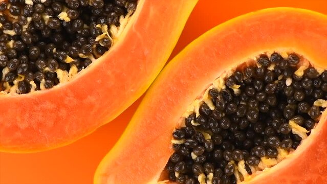 Papaya fruits on orange, yellow color background. Halved fresh organic Papaya exotic fruit design, close up. Top view, rotating