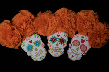 Cookies with shapes of Mexican catrinas and orange marigold flowers to celebrate Halloween or Day of the Dead on black background