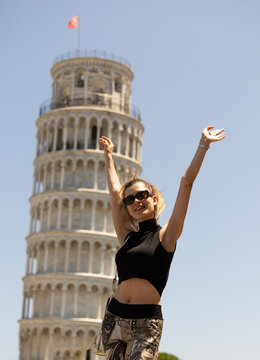Happy young woman with her hands raised in front of the Leaning Tower of Pisa.